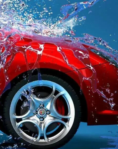 Professional washer in blue uniform washing luxury car with water gun on an open air car wash. Close up photo.